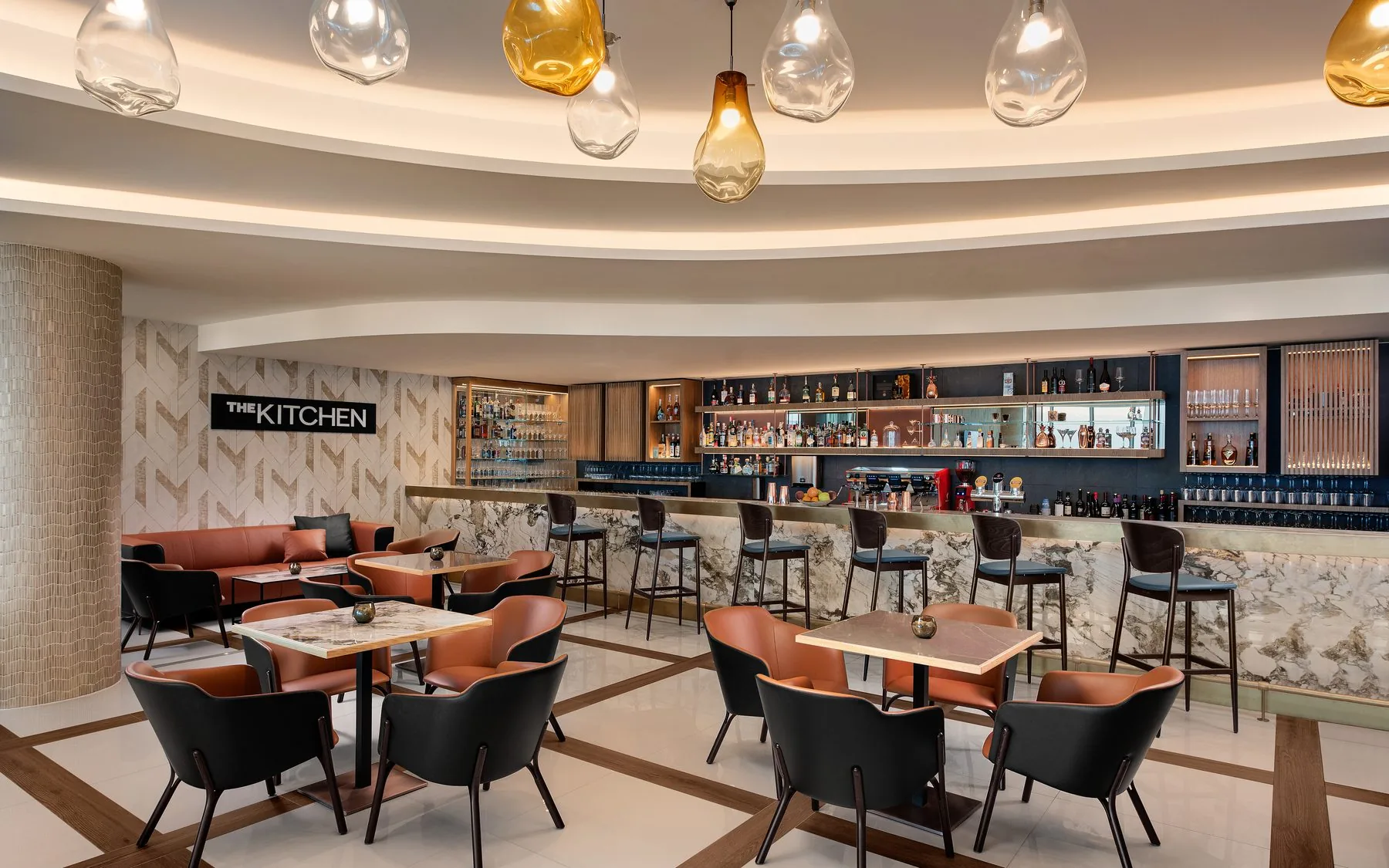 Bar di un hotel: bancone rivestito in lastre di marmo chiaro a venatura continua, tavolini con piano in marmo