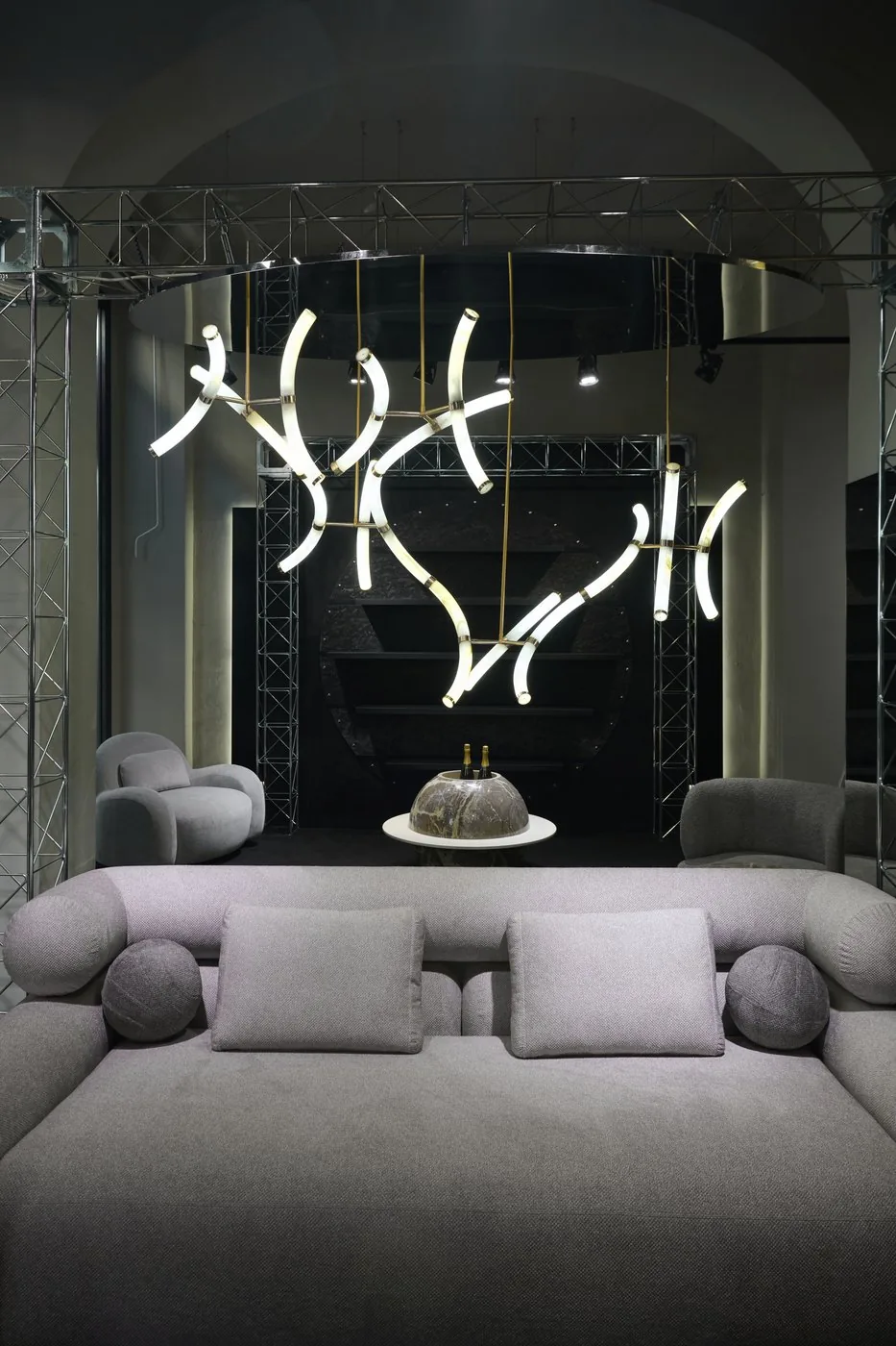 La lampada LuxOnyx accesa e sospesa sopra un salotto, con Parione e la libreria Monti sullo sfondo